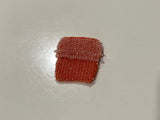 Small orange bead knitted bag on a white surface with tiled floor in the background
