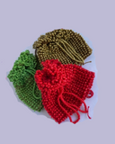 Three beaded pouch bags in red, green, and gold on a light grey background