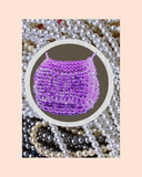 Purple beaded necklace bag surrounded by pearls on a beige background
