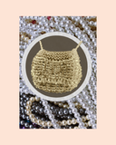 Beige bag necklace surrounded by pearls and a pastel background