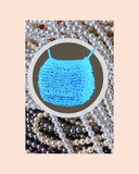 Blue bead knitted bag surrounded by pearls and a pastel background