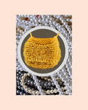 Golden beaded bag necklace surrounded by pearls on a pink background