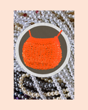 Orange bead knitted bag necklace surrounded by pearls on a pastel background