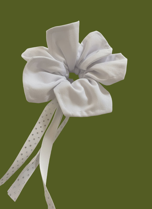A black open flower like mini bag with a black bow with a polka dot ribbon on a textured beige background