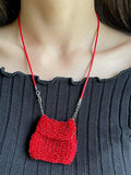 Red beaded necklace with a small pouch bag on a person wearing a dark gray top.