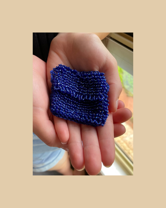 Hand holding a blue textured mini bead knitted bag against a beige background