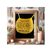 A promotional image featuring a gold bead knit bag necklace displayed in a frame, with various decorative items and candles arranged around it, indicating a craft or workshop setting.