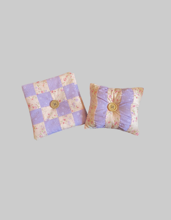 Pin Cushion and Needle Holder Set Two small pastel fabric pieces with buttons on a textured surface,  encouraging a patchwork project.