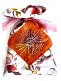 Hand sewn material pouch with a ribbon tie and a brown square of bead embroidery with different shades of beads on a white background